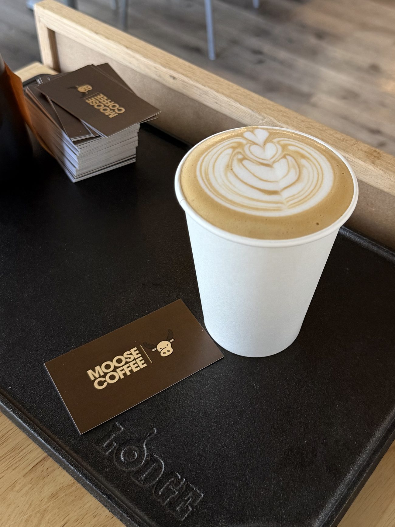 A hot latte with rosetta latte art beside a Moose Coffee card